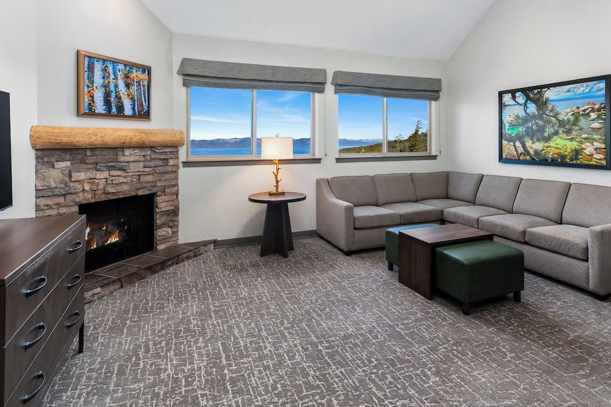 A living room with a stone fireplace, a sectional sofa, a small table, and a TV.