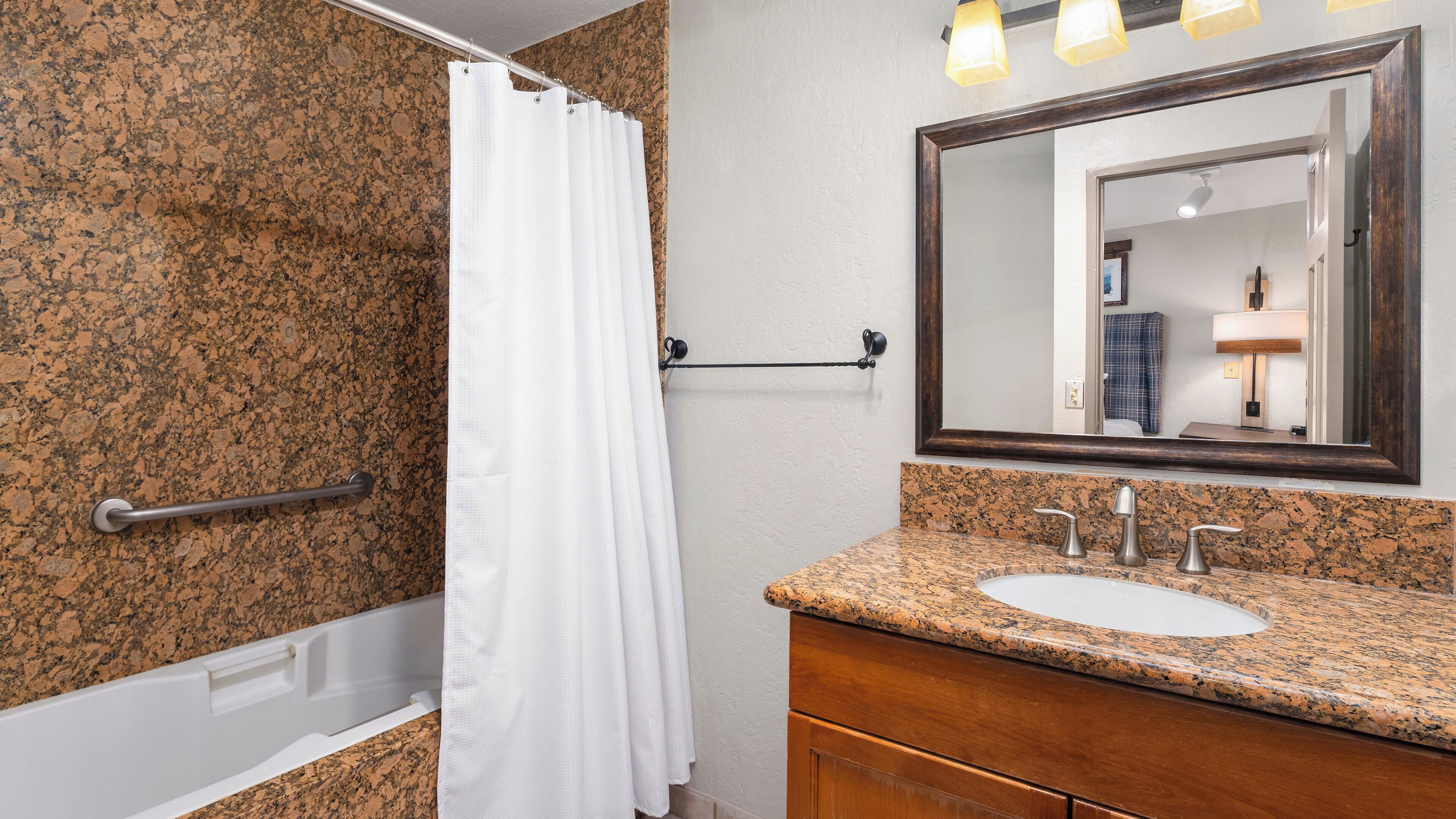 A bathroom with a granite countertop, a white sink, a mirror, and a shower curtain.