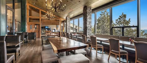 Un restaurant spacieux avec de hauts plafonds, un lustre et de grandes fenêtres donnant sur la verdure.