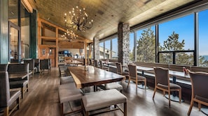 A spacious restaurant with high ceilings, a chandelier, and large windows offering a view of trees.