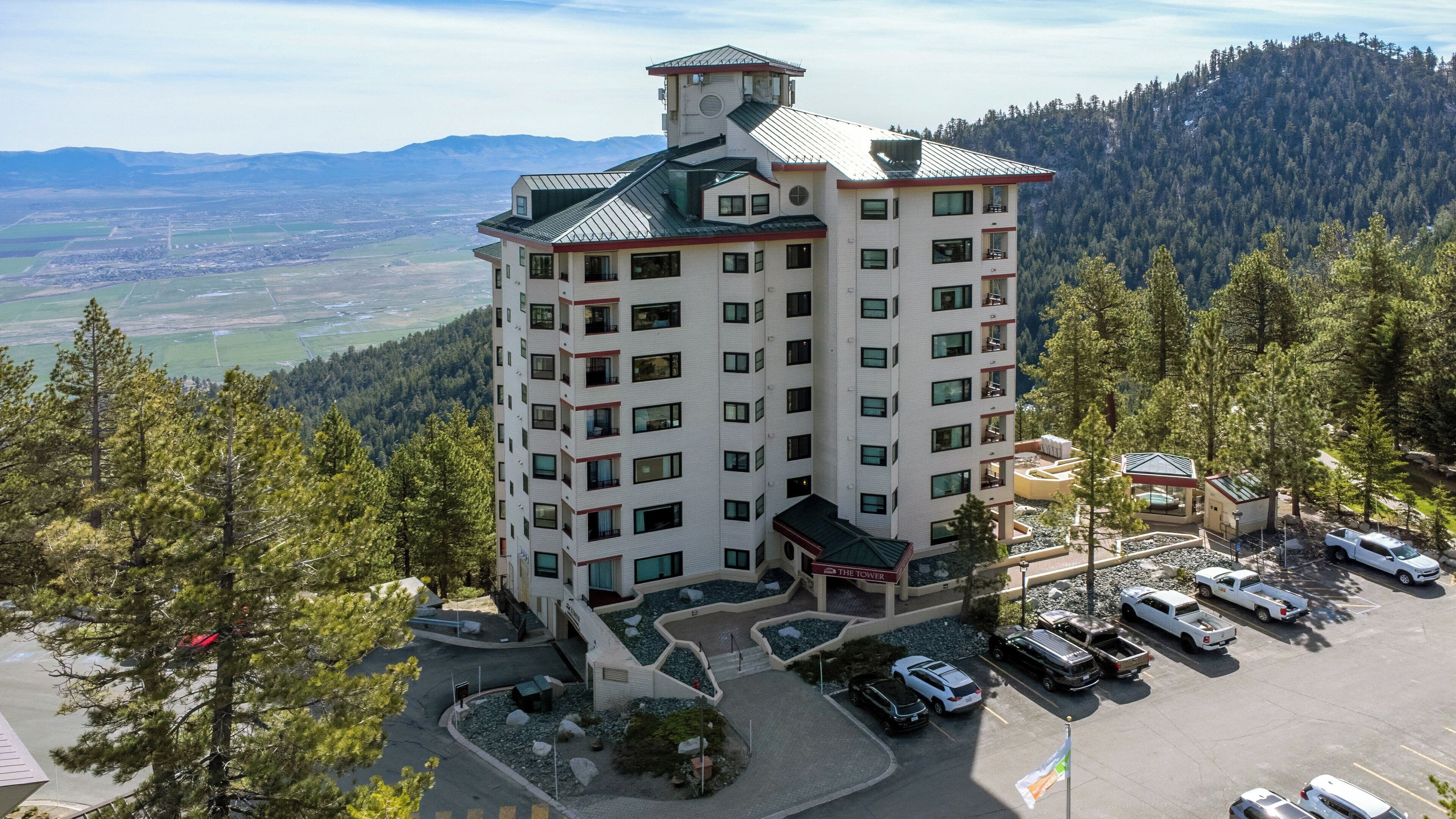 Un hotel de varios pisos con un patio central, zona de estacionamiento y vistas del paisaje circundante.