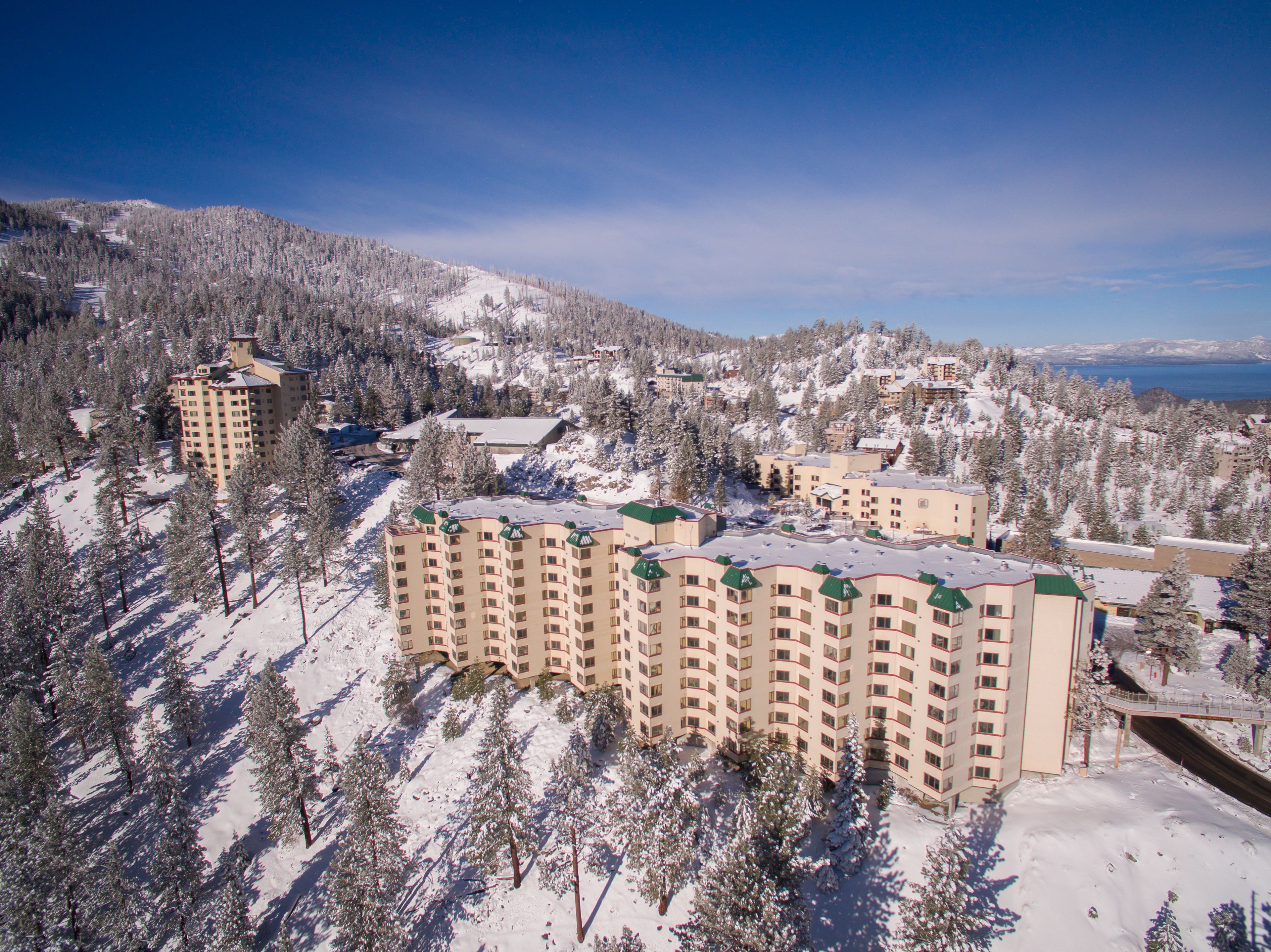 A snow-covered resort with multiple buildings, including a prominent hotel with a curved facade and a ski lift visible in the background.