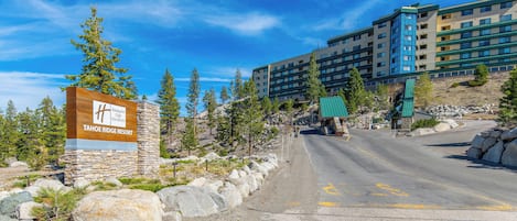A sign for Tahoe Bridge Resort, a multi-story building with a modern design, and a paved road leading to it.