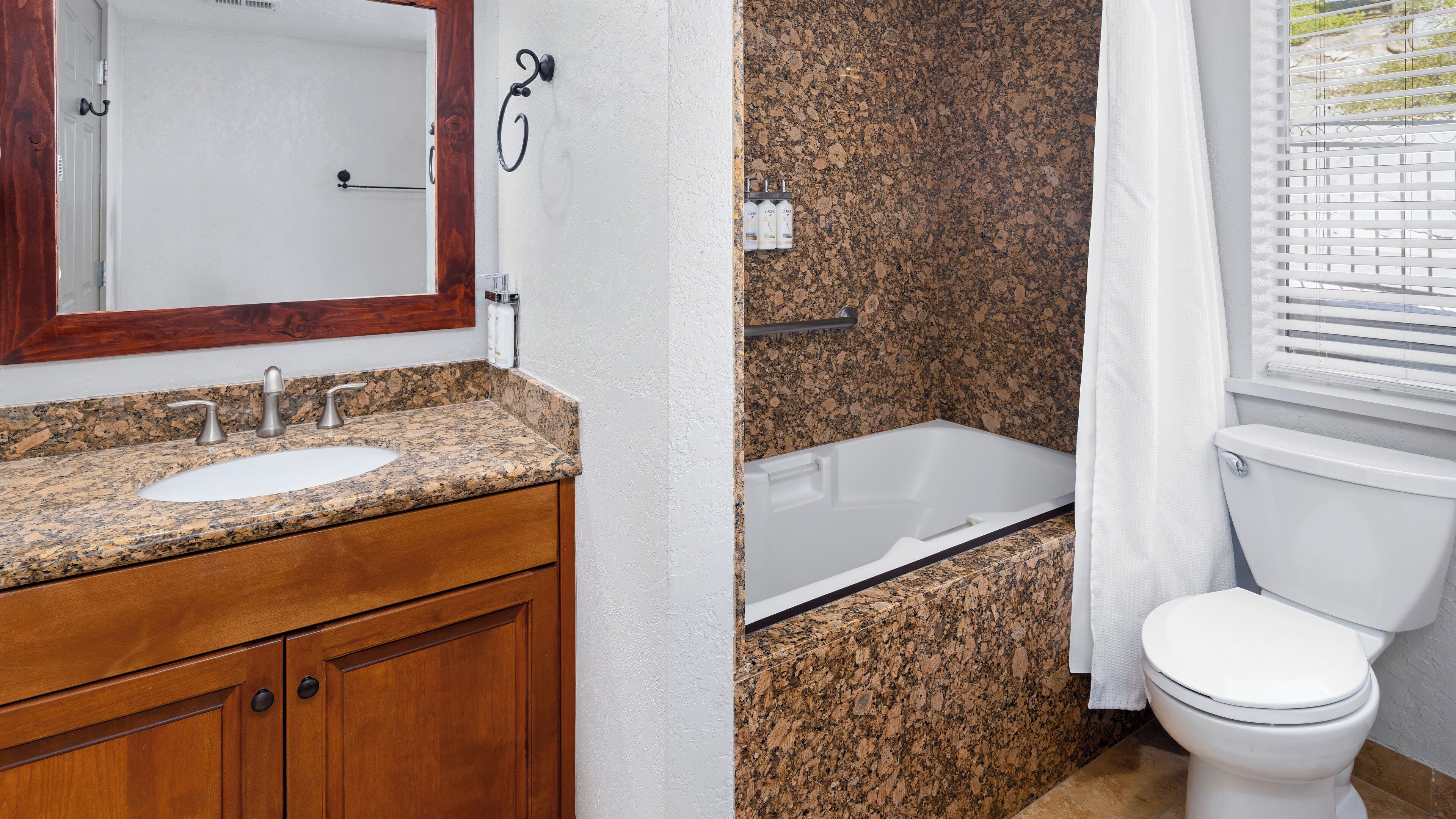 Une salle de bain avec un lavabo en granit, un meuble-lavabo en bois, des toilettes blanches et une baignoire.
