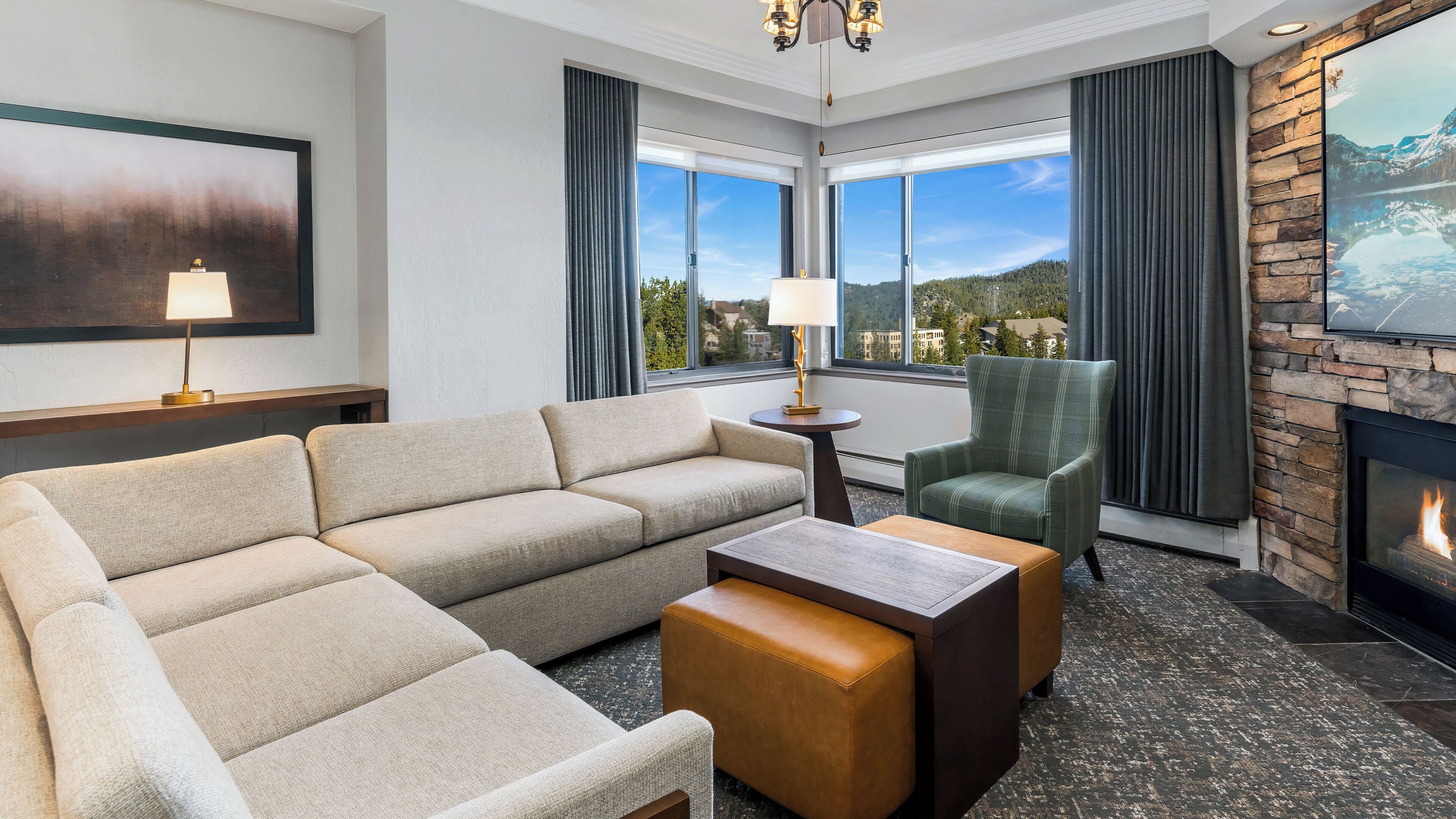 A hotel room with a sofa, armchair, coffee table, lamp, fireplace, and large windows with a view.