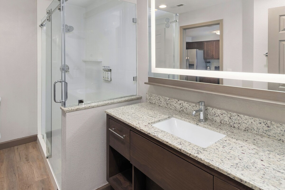 A bathroom with a glass-enclosed shower, a white toilet, a granite countertop sink, and a mirror above the sink.