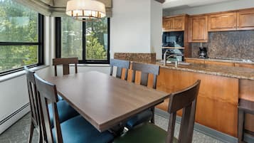 Un comedor con mesa y sillas, una ventana con vistas a árboles, y una cocina con alacenas de madera y encimeras de granito.