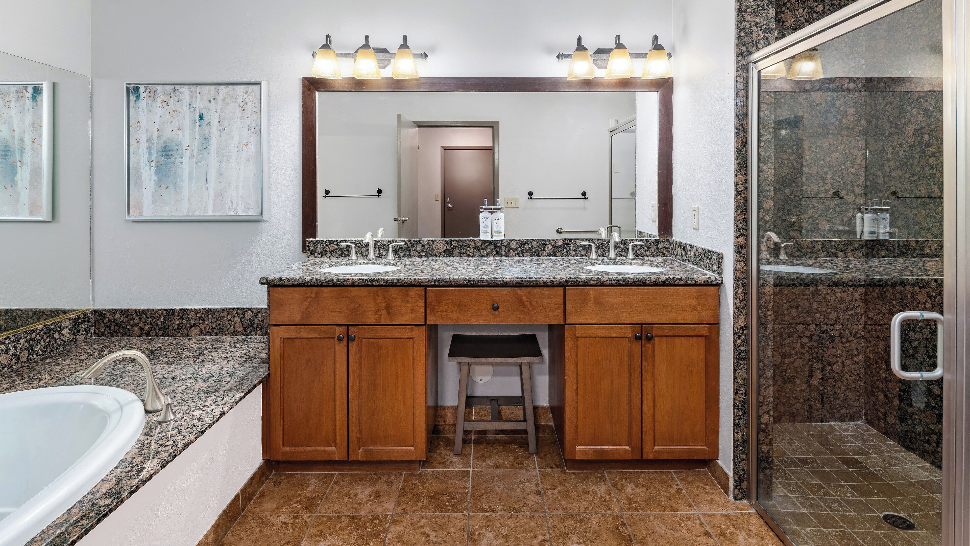 Une salle de bain avec un meuble-lavabo à deux vasques, un miroir avec éclairage intégré, un espace douche et des toilettes.