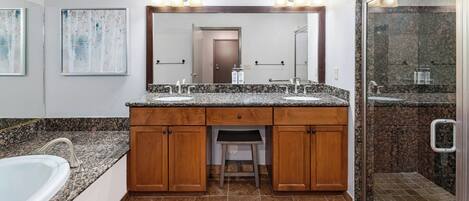 A bathroom with a double sink vanity, a mirror with lights, a shower area, and a toilet.