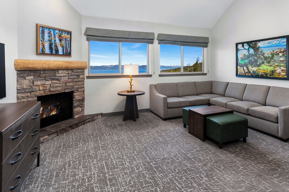 A living room with a stone fireplace, a sectional sofa, a small table, and a TV.