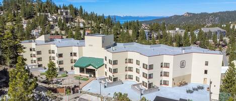 A multi-story hotel with a green-roofed building, a parking lot, and a mountainous backdrop.