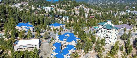 A mountainous resort with multiple buildings, including a large hotel with a blue roof, surrounded by dense forest and a view of a lake.