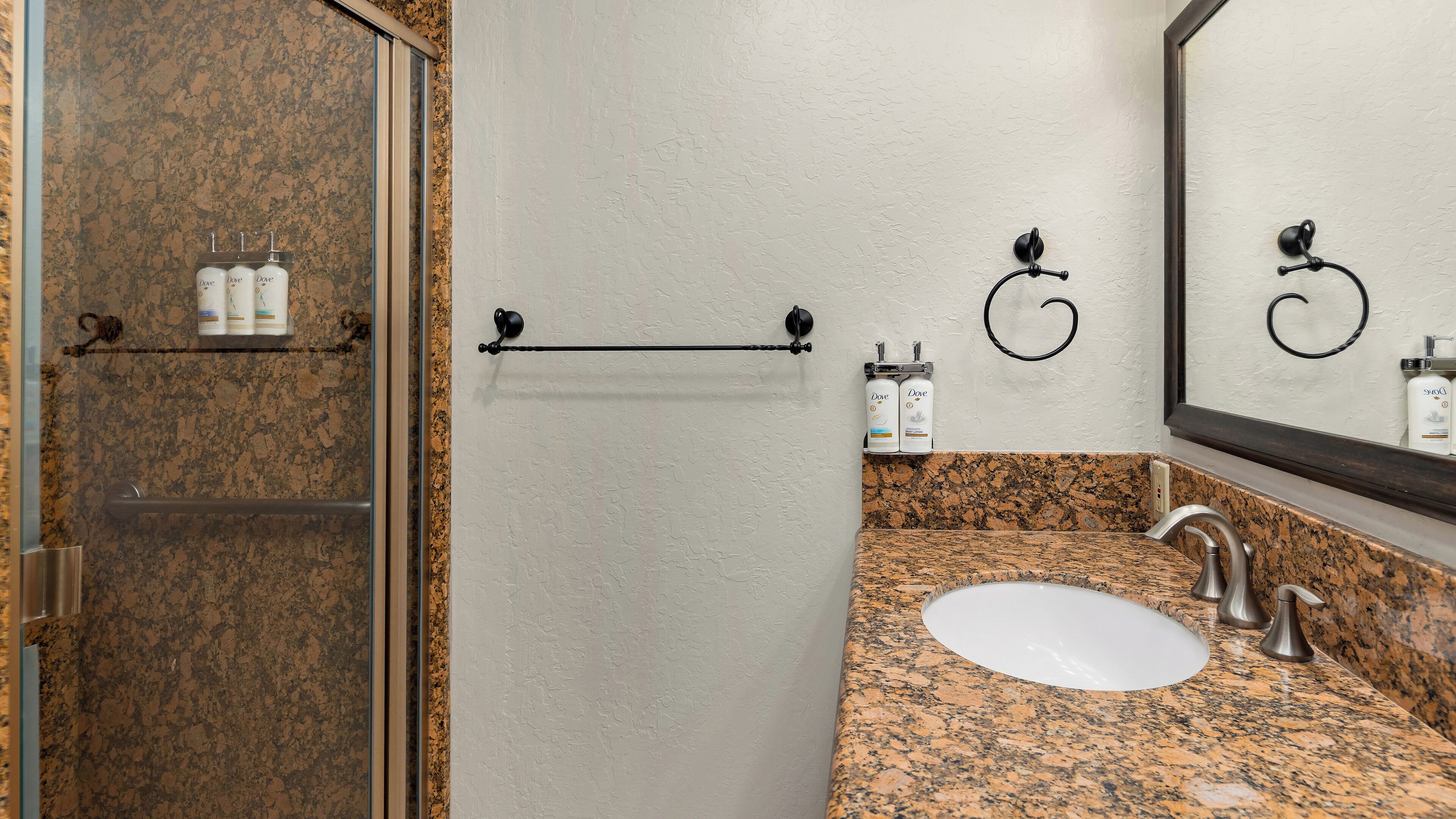 A bathroom with a granite countertop, a white sink, a mirror, and toiletries on a shelf.