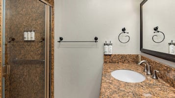 A bathroom with a granite countertop, a white sink, a mirror, and toiletries on a shelf.