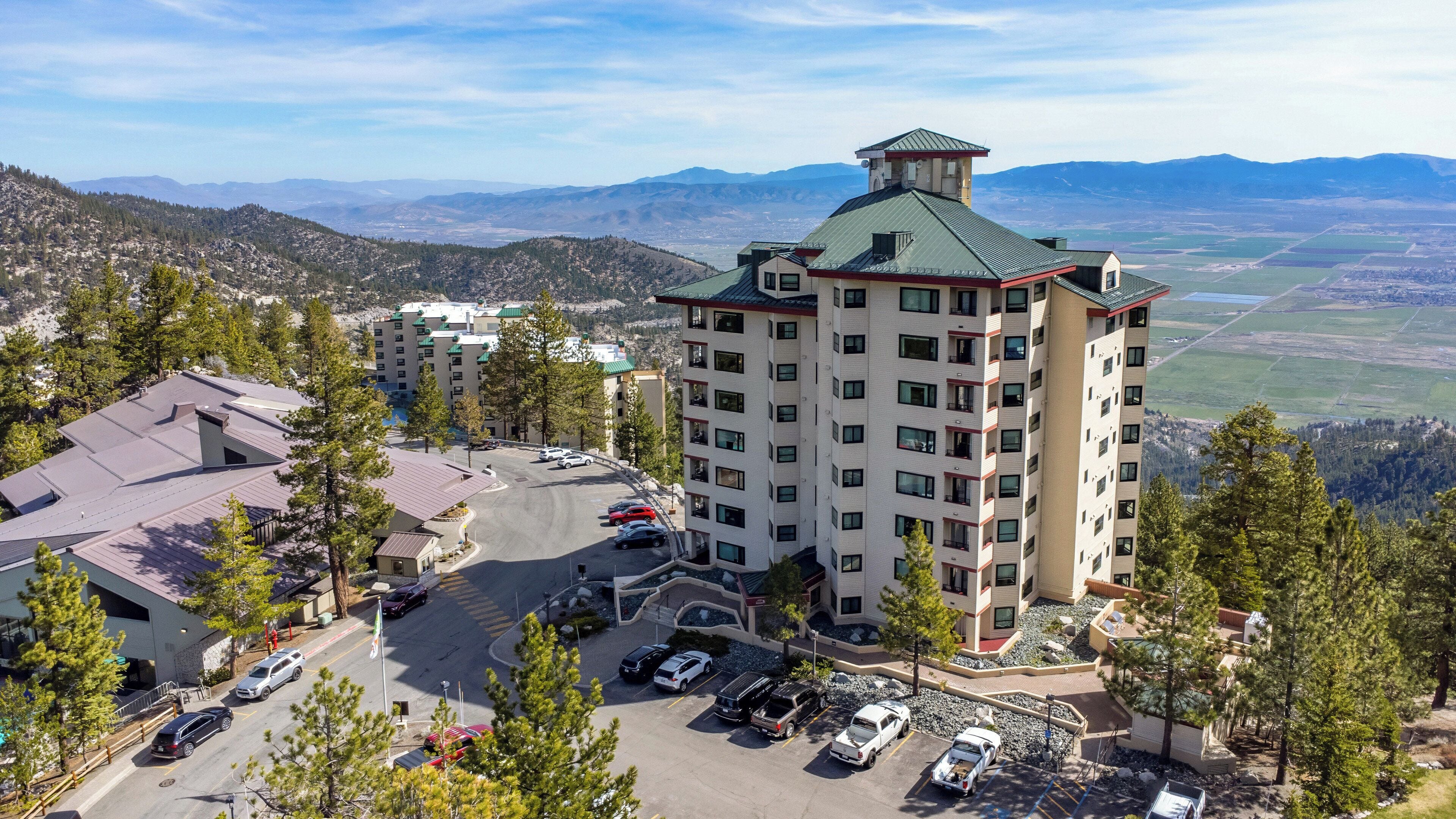 Un hôtel à plusieurs étages doté d’un parking, entouré de montagnes et d’arbres.