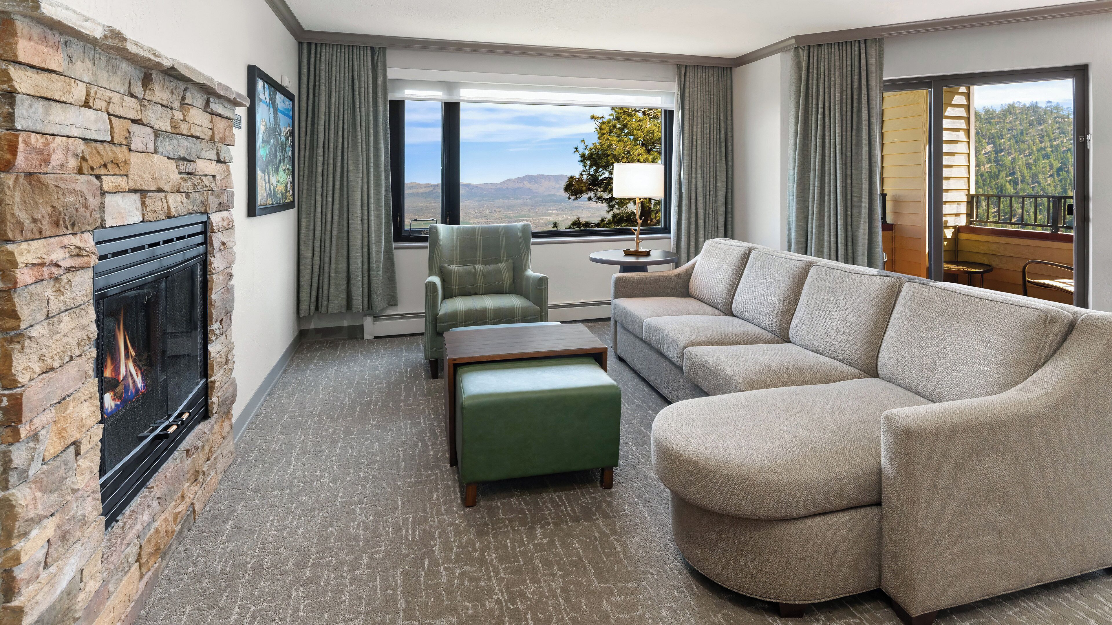 A living room with a fireplace, a sofa, a chair, and a view of the mountains.