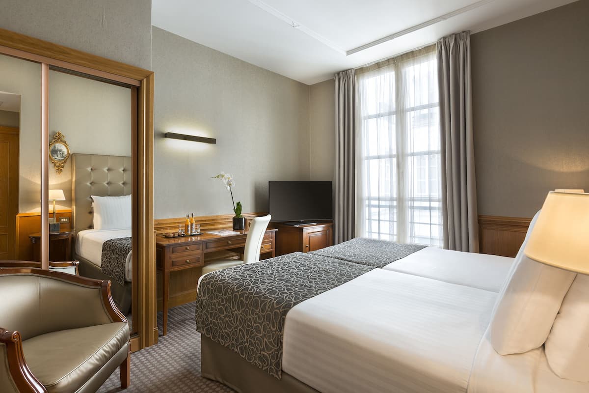 A hotel room with a bed, a desk, a chair, a television, and a large mirror.