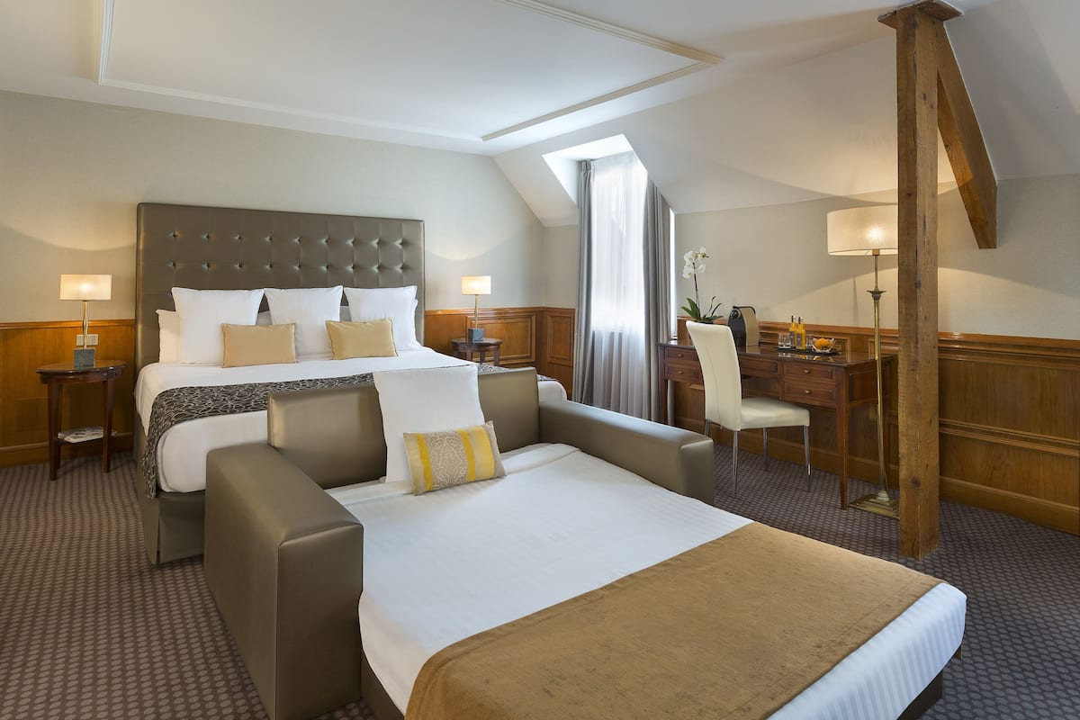A hotel room with a large bed, two armchairs, a desk, and a lamp.