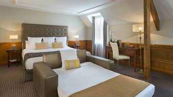 Une chambre d’hôtel avec un grand lit, deux fauteuils, un bureau et une lampe.