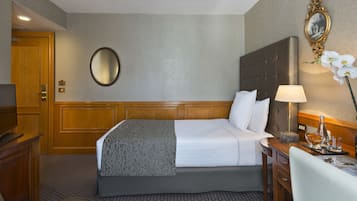 A hotel room with a large bed, a wooden desk, a chair, a mirror, and a lamp.