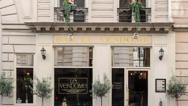 Fachada de un edificio con un letrero que dice "BAR LE VENDOME" y un amplio ventanal donde se ve el nombre "Le Vendome" y "Bar de Cócteles".