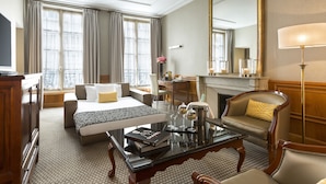 Habitación de hotel con cama, sofá, mesa de centro, sillón, chimenea y un espejo grande.