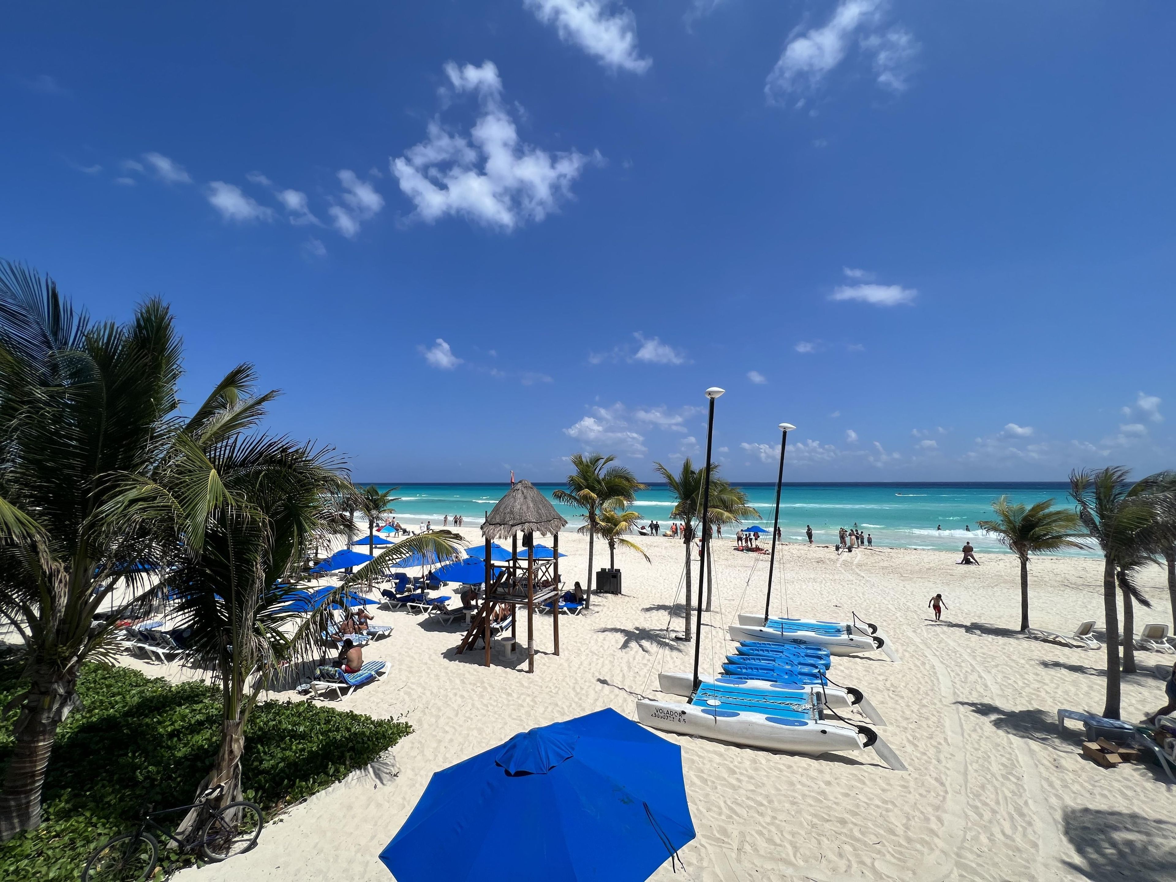 A beach with lounge chairs, umbrellas, and a thatched structure.