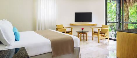 A hotel room with a bed, a TV, a seating area with chairs, a small table, and a large window with a view of trees.