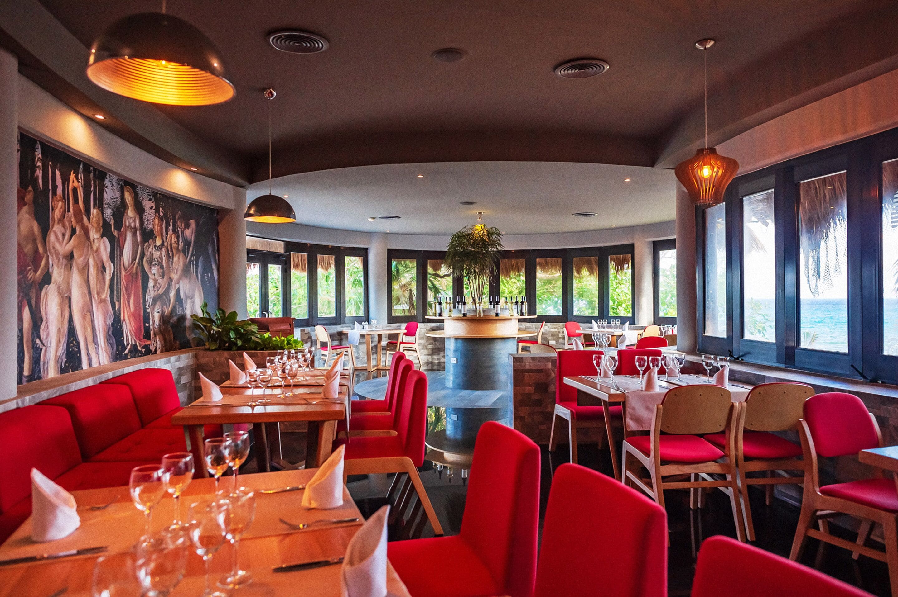 Un restaurante con asientos rojos, una barra central y grandes ventanales que ofrecen vistas al exterior.