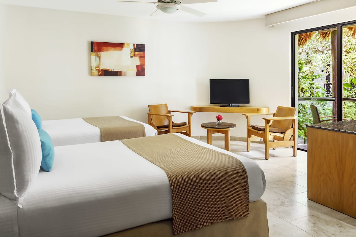 A hotel room with two beds, a TV, a small table, and chairs.