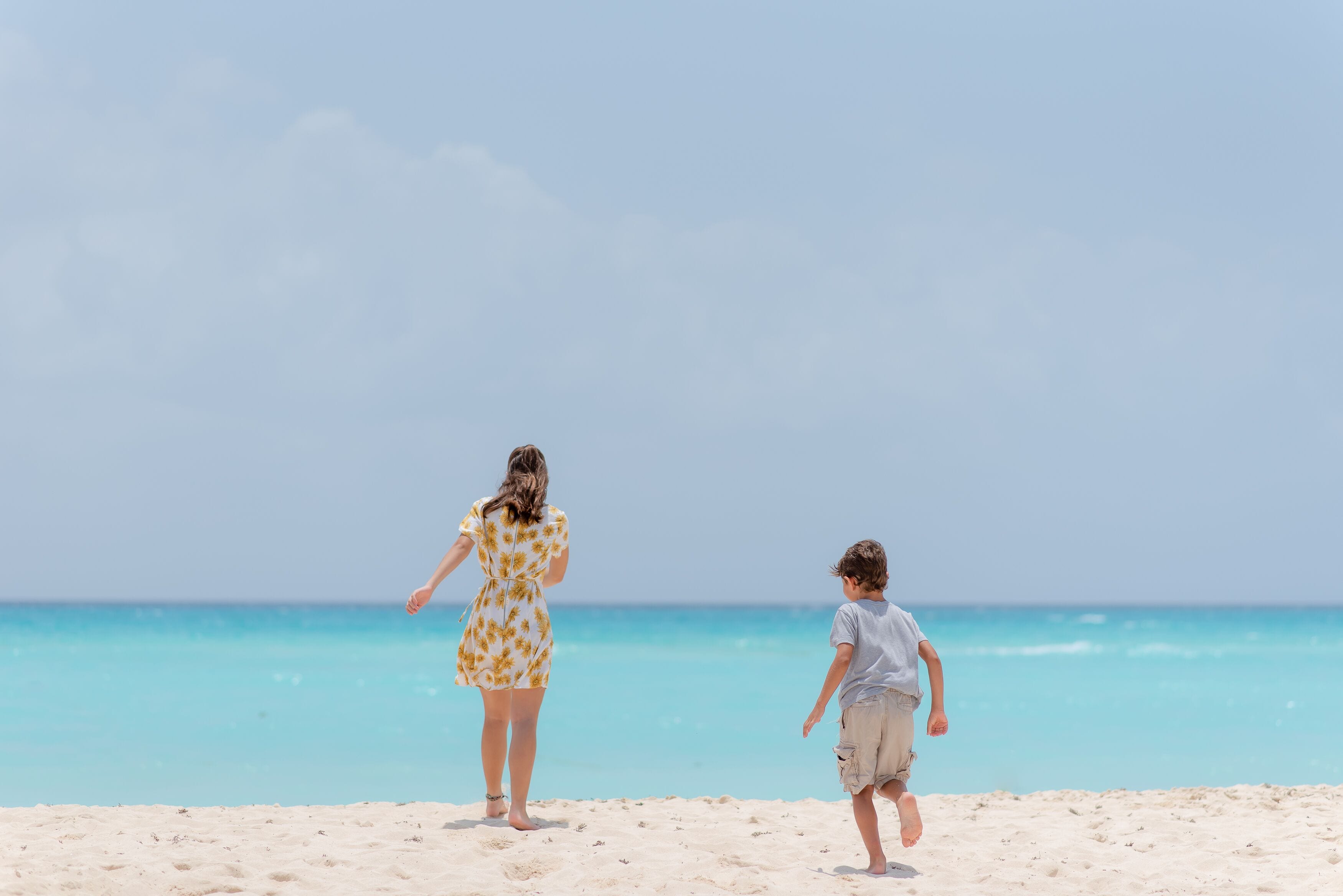 Une scène de plage avec une femme portant une robe à motifs floraux et un enfant en short.