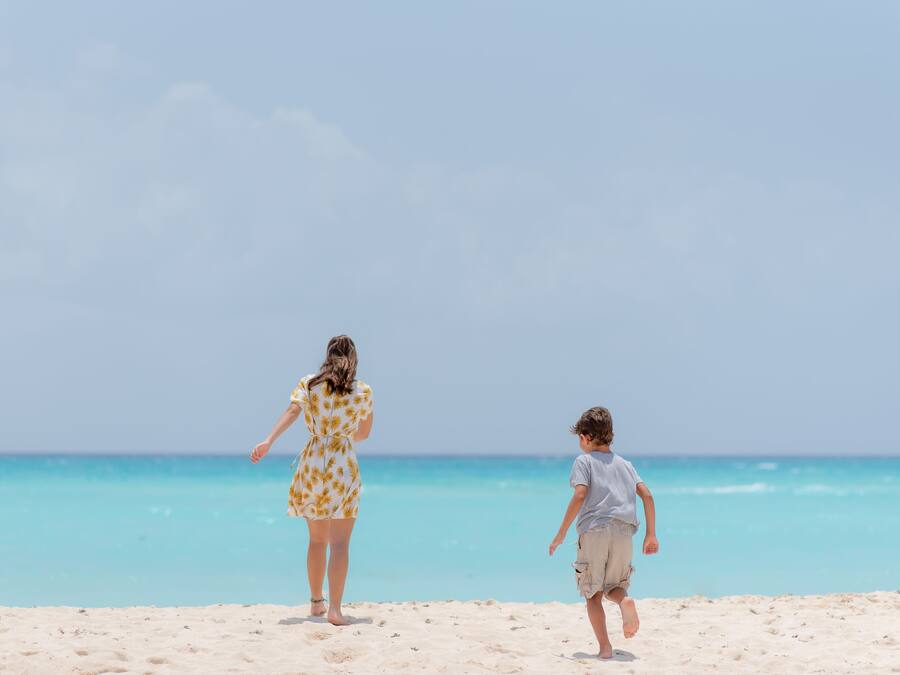 A beach scene with a woman in a floral dress and a child in shorts.