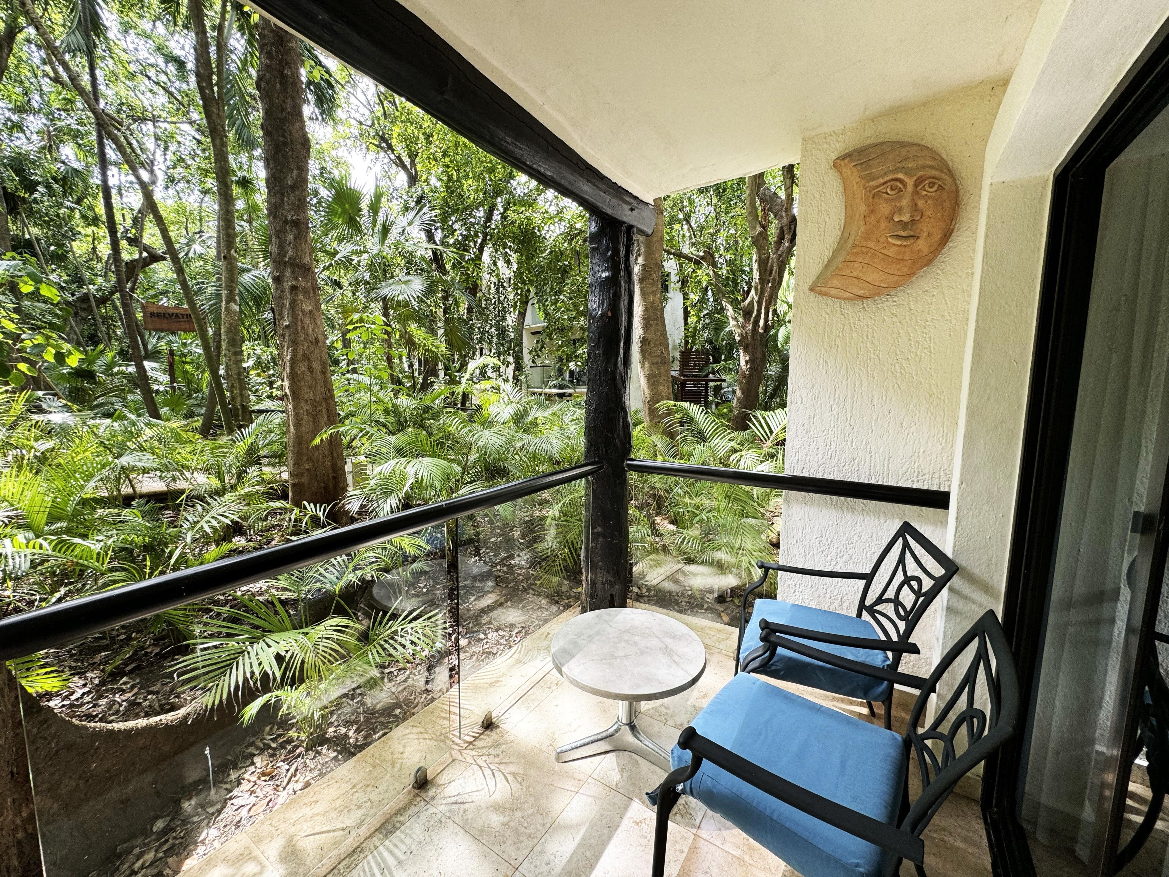 A balcony with a glass railing, a round table, and two blue chairs.