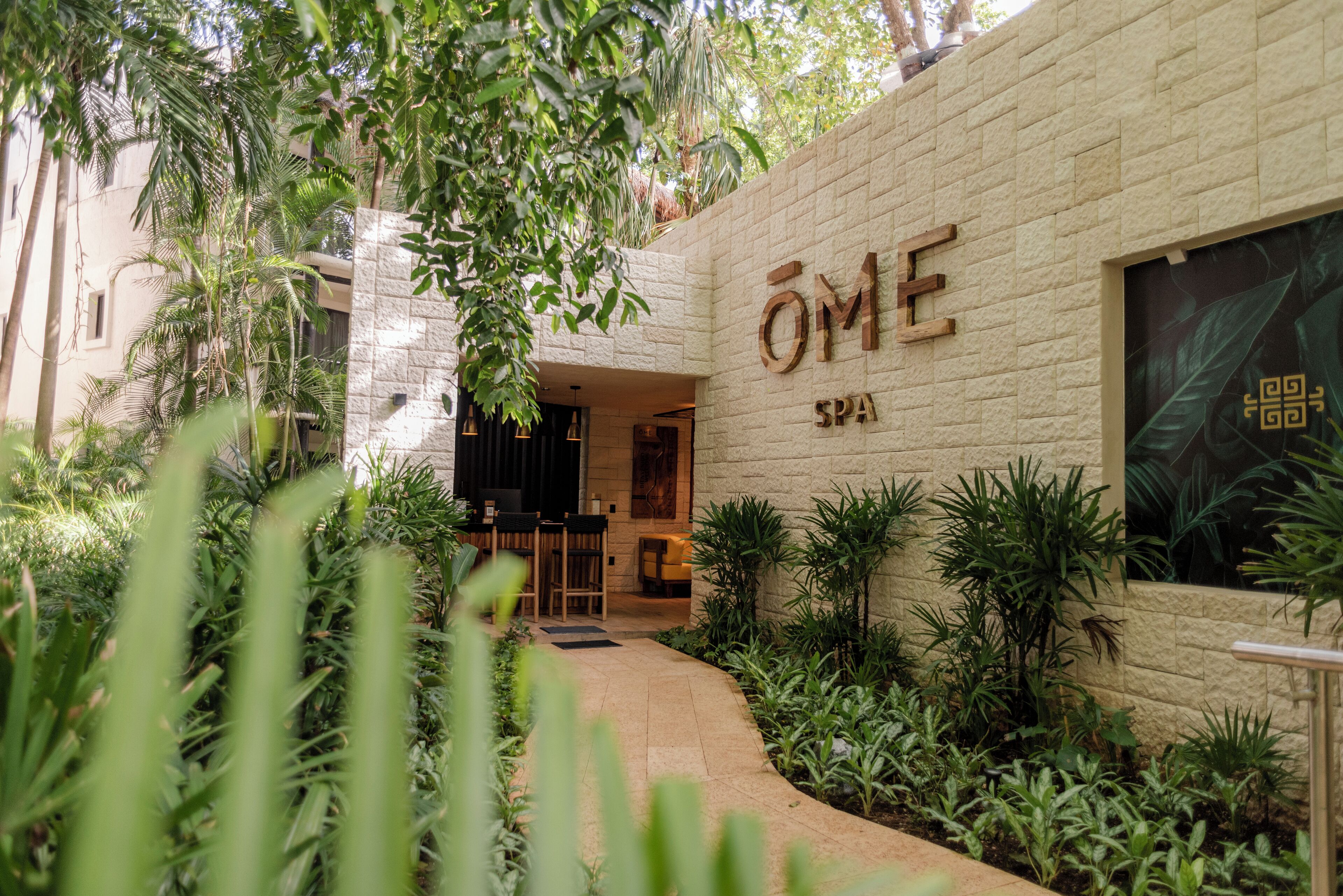 Entrada de un spa con pared de piedra, zona de estar interior y abundante vegetación.