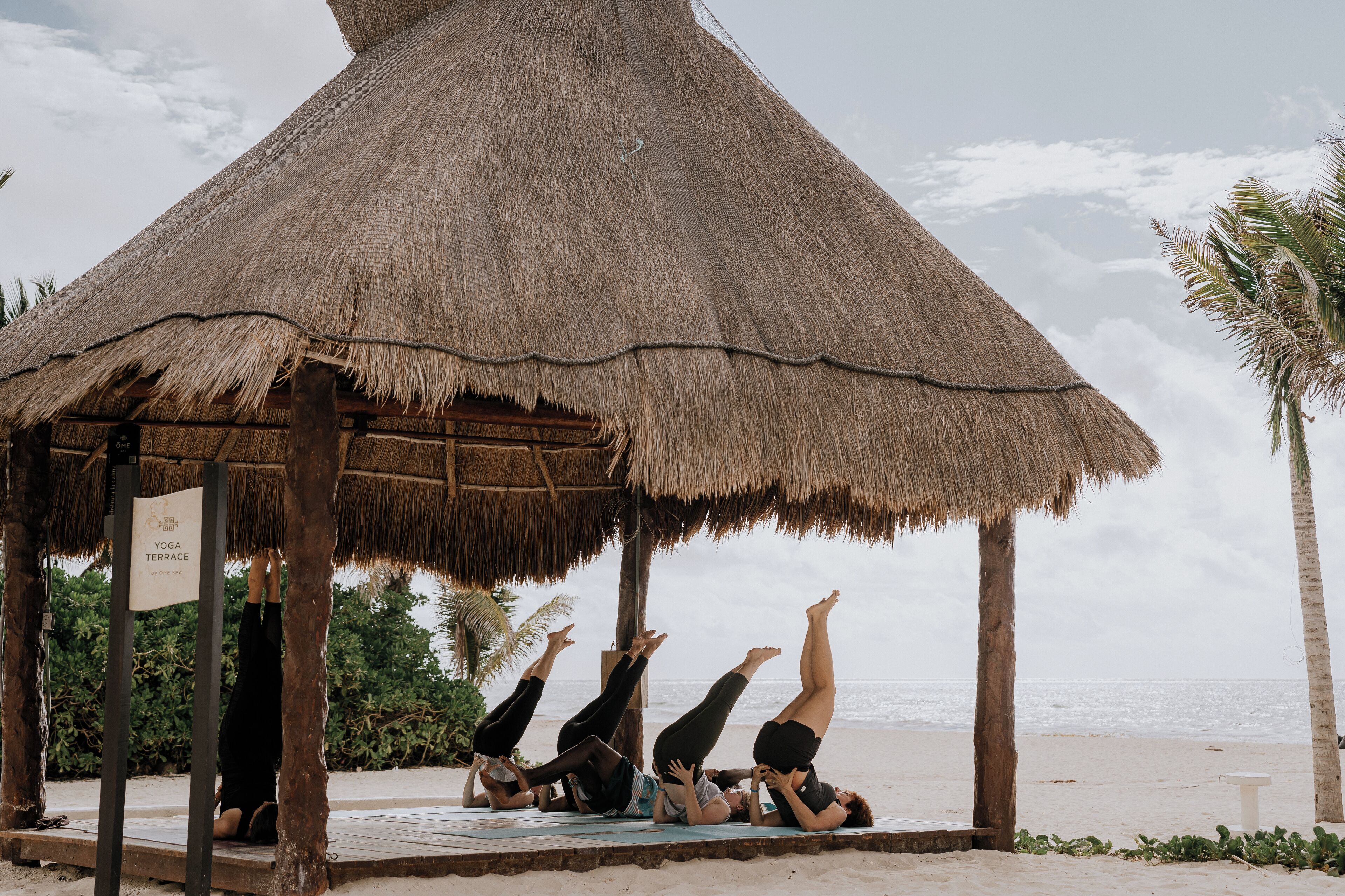 A thatched-roof structure on a beach with people practicing yoga.