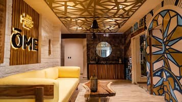 Um saguão moderno com um sofá amarelo, um balcão de recepção de madeira e uma parede com padrão geométrico.