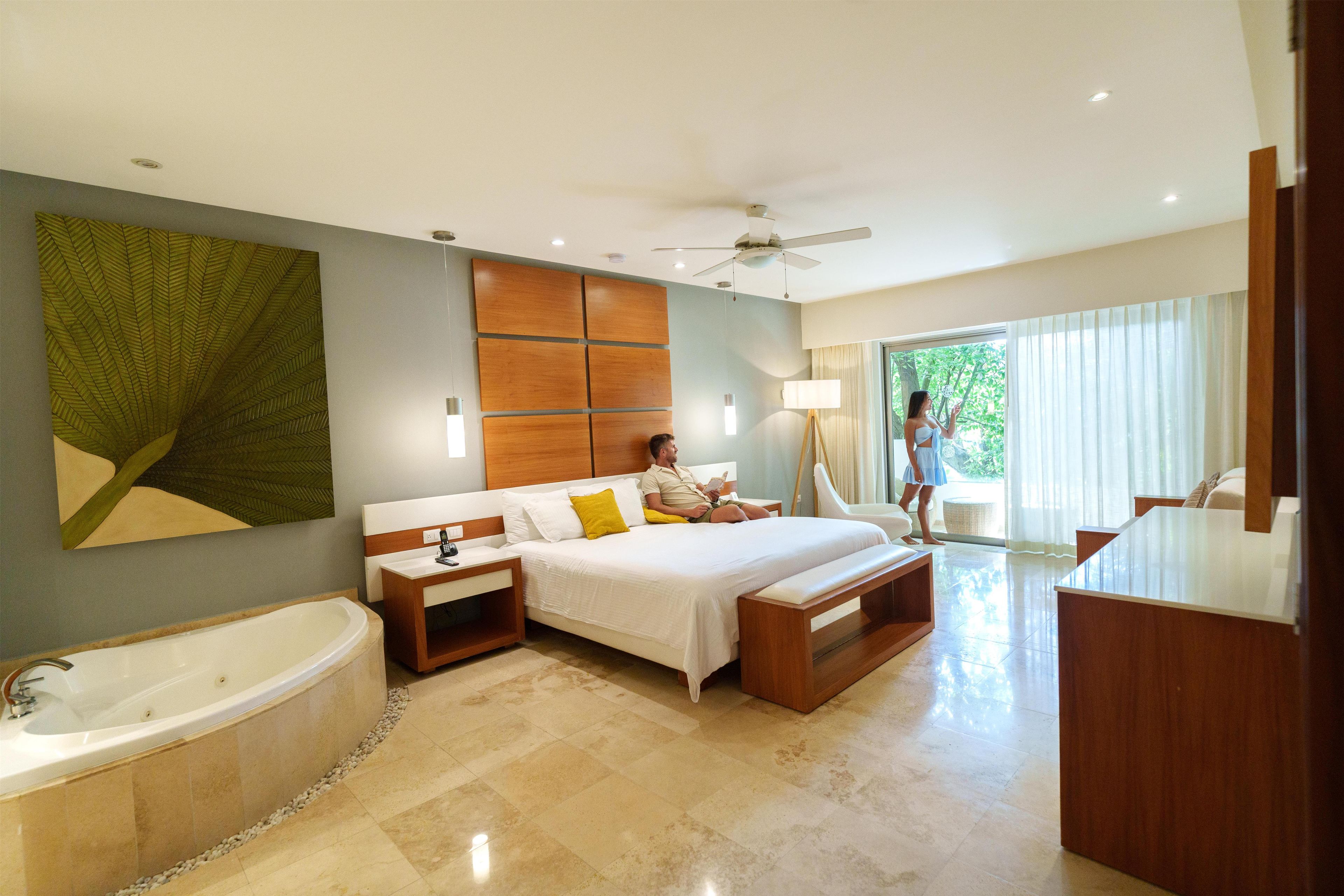 A hotel room with a large bed, a separate sitting area, a bathtub, and a view of the outdoors.