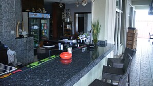 A modern kitchen with a black granite countertop, a refrigerator stocked with beverages, and a dining area with wicker chairs. - Travel Inn Hotel (Simpson Bay)