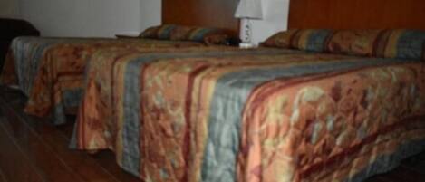 A hotel room with two beds, wooden headboards, and a nightstand with a lamp.
