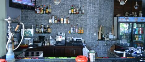 A bar with a brick wall, shelves of liquor bottles, a television, and a coffee machine.