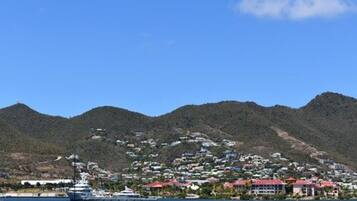 A coastal town with a marina, houses with red roofs, and hills in the background.