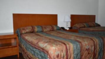 Una habitación con dos camas, cabeceros de madera y una mesita de noche con lámpara.