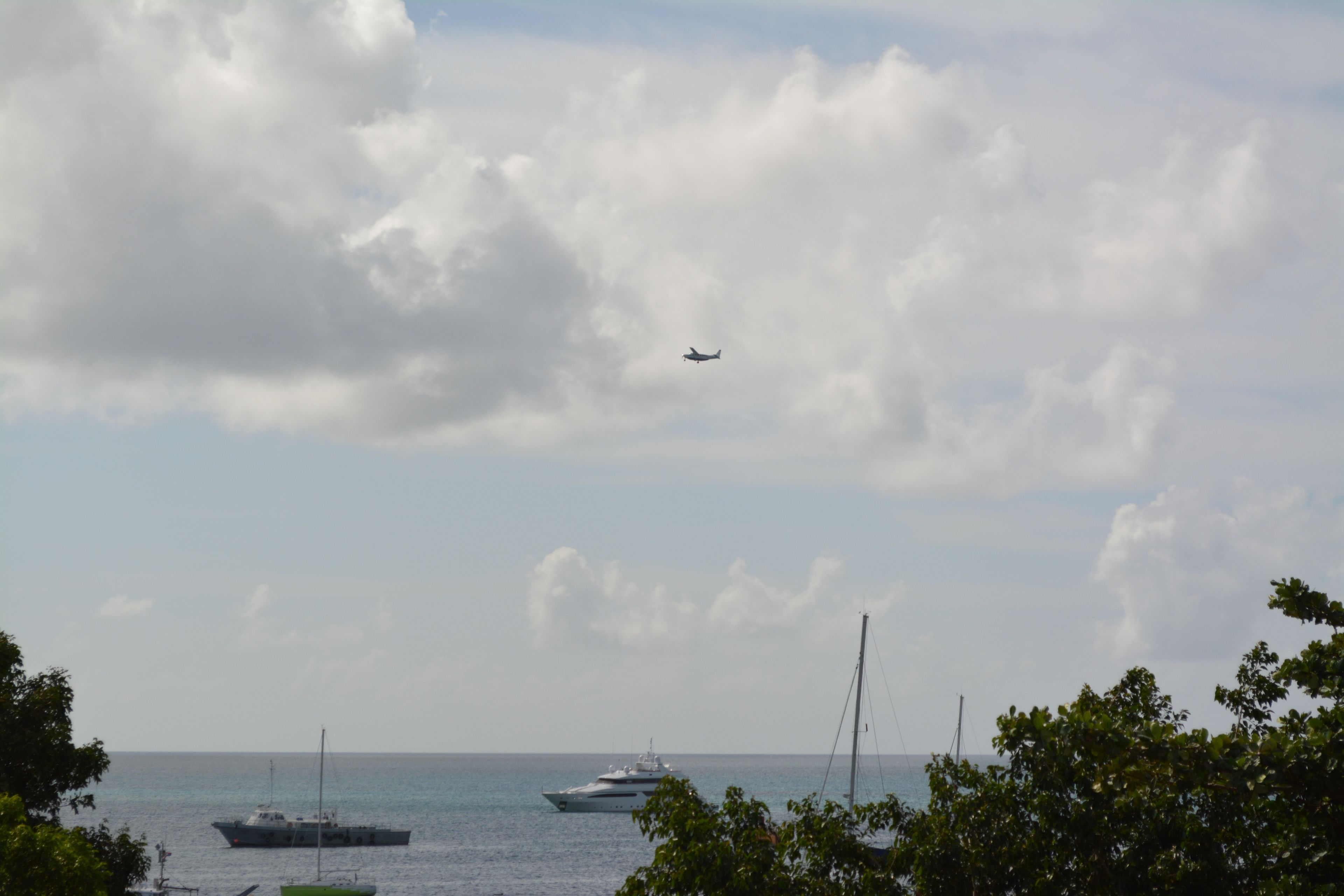 A view of the sea with boats and a plane in the sky.