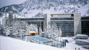 Un edificio moderno con piscina, rodeado de árboles nevados y montañas.