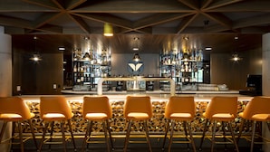 Zona de bar con pared de diseño geométrico, barra central y varias lámparas colgantes.