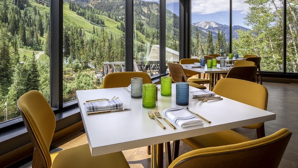 Comedor con una mesa dispuesta para dos, amplias ventanas con vistas a la montaña y sillas modernas.
