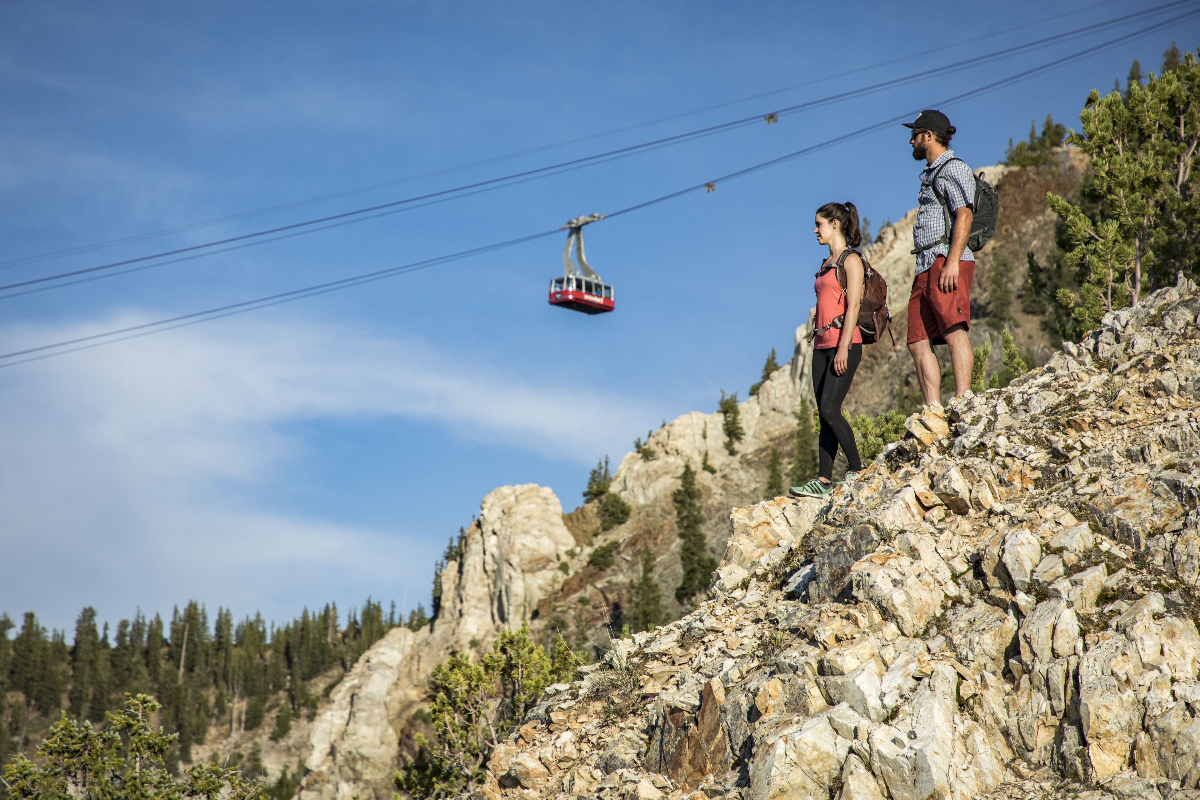 Un teleférico avanza sobre terreno rocoso con excursionistas en un sendero de montaña.