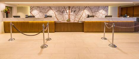 Una zona de recepción con mostrador de mármol, un mostrador de madera y una pared con diseño arbóreo.