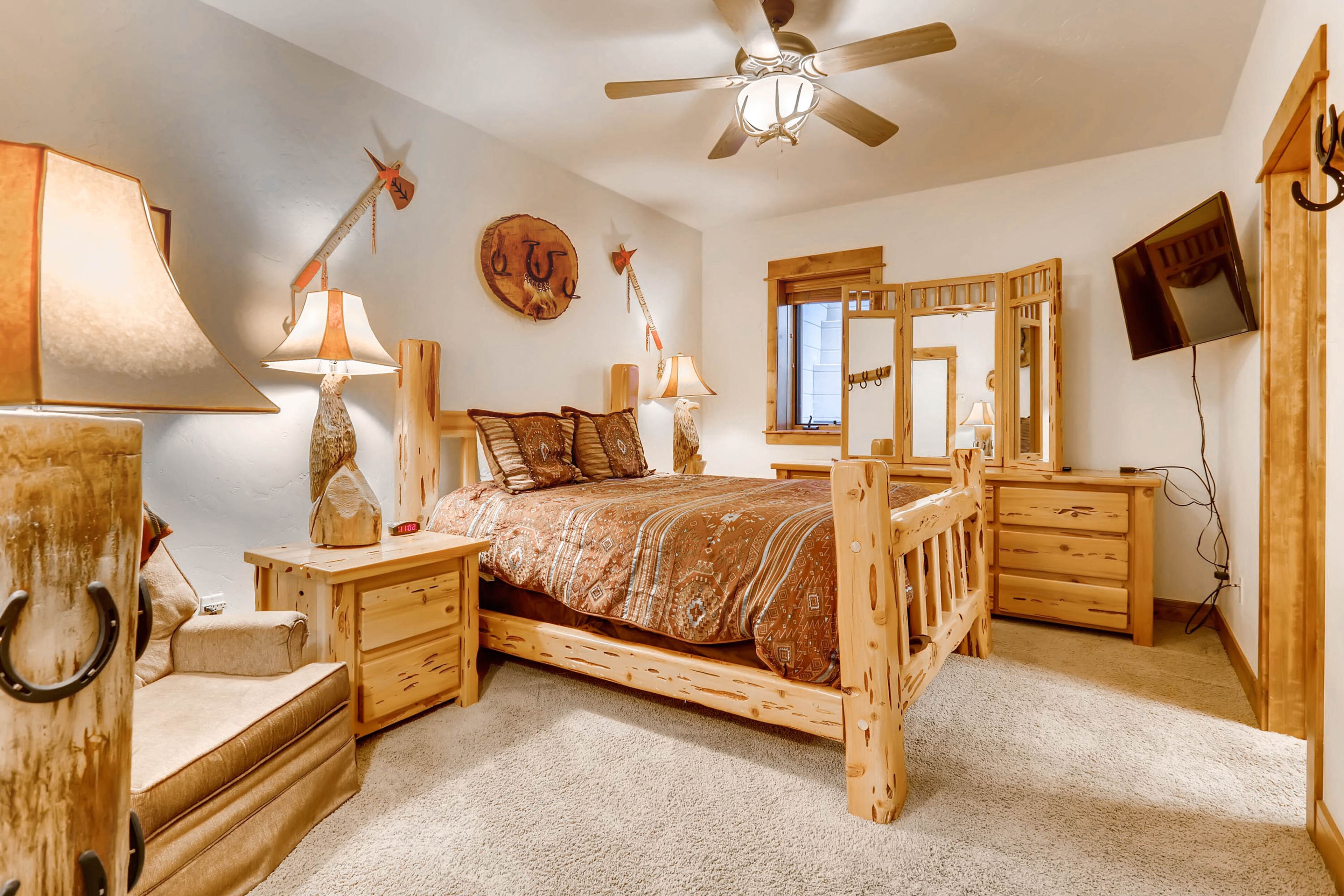 Un dormitorio con una cama de madera, dos mesitas de noche con lámparas, un espejo y un ventilador de techo.
