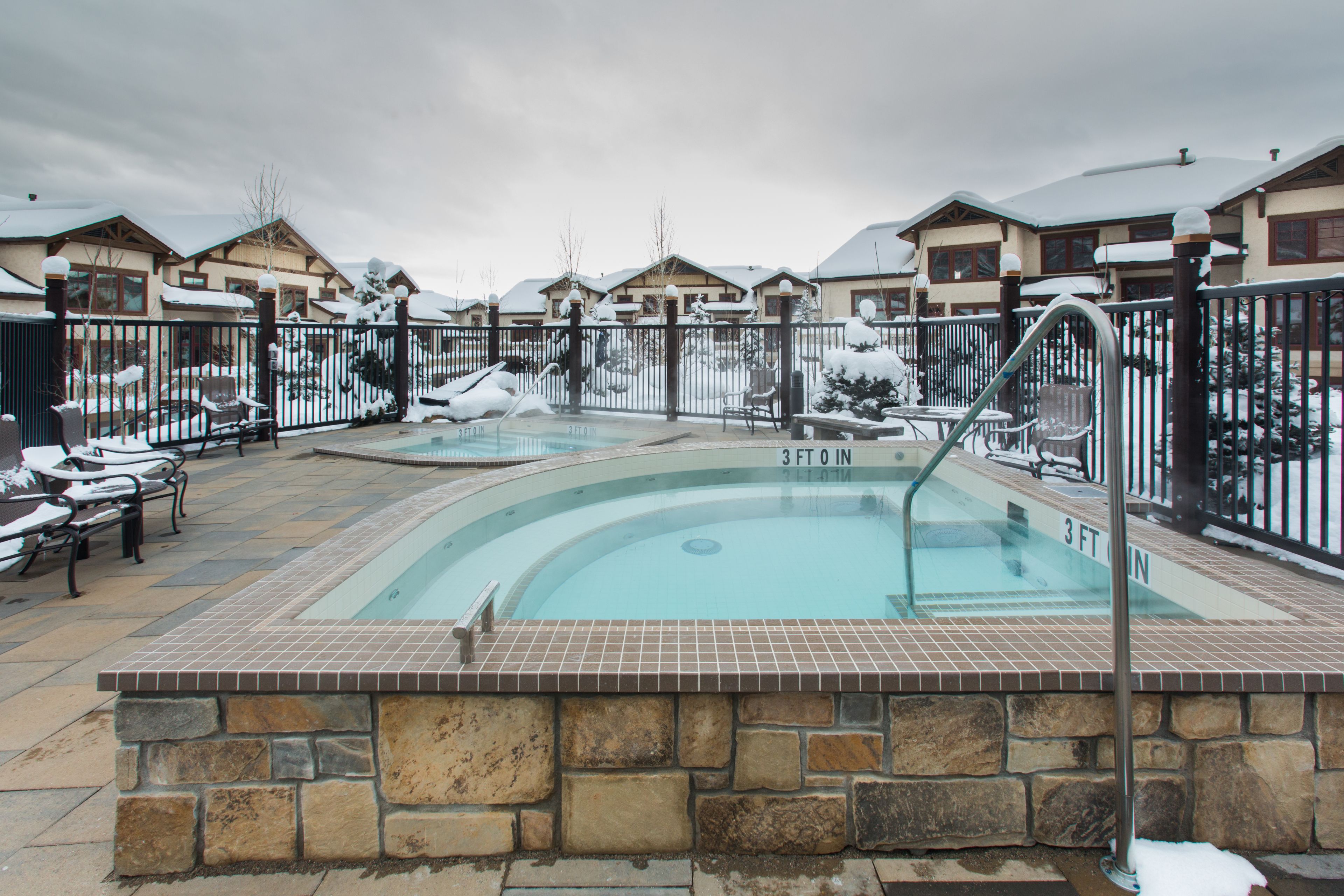 A pool area with stone tiles and a 3-foot depth marker, surrounded by lounge chairs and a fence.